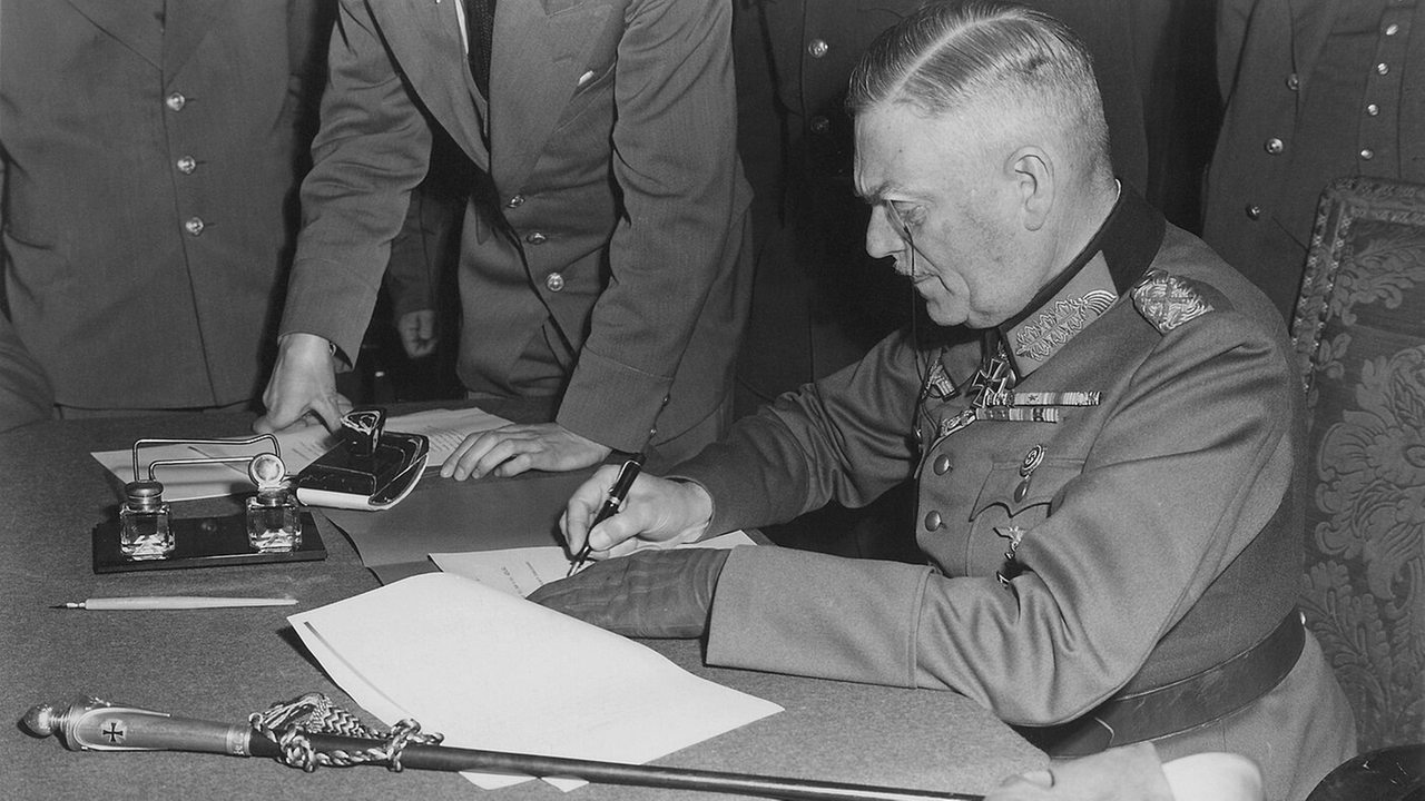 Generalfeldmarschall Keitel sitzt an einem Schreibtisch und unterzeichnet die Kapitulationserklärung des Dritten Reichs