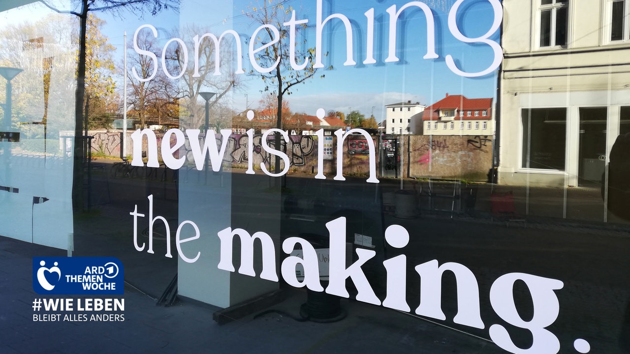 Werbung "Something is in the making" an einer Fensterscheibe in der sich Häuser spiegeln