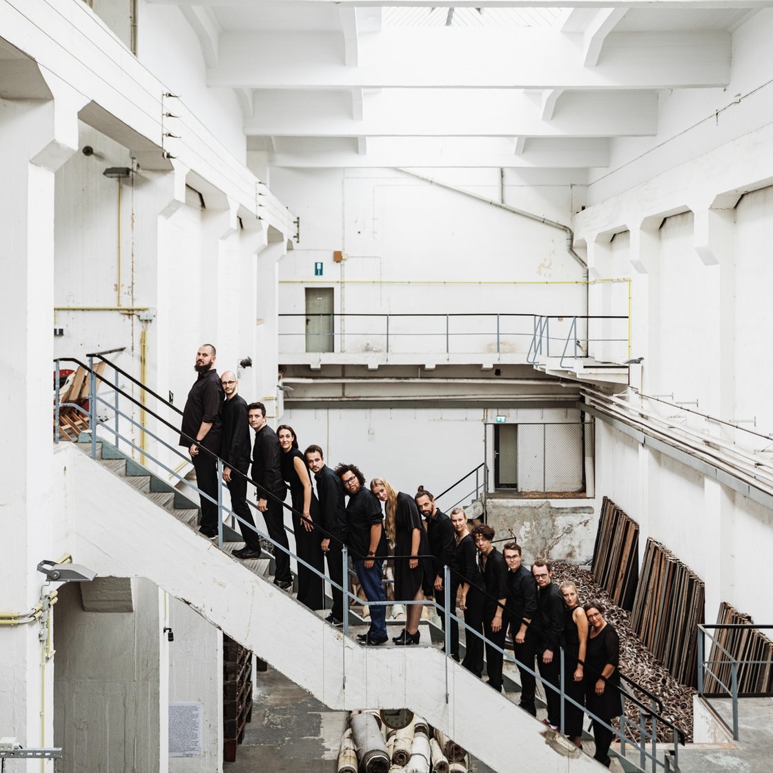 Vierzehn Menschen in schwarzen Kleidung stehen in einer Reihe auf einer Treppe 