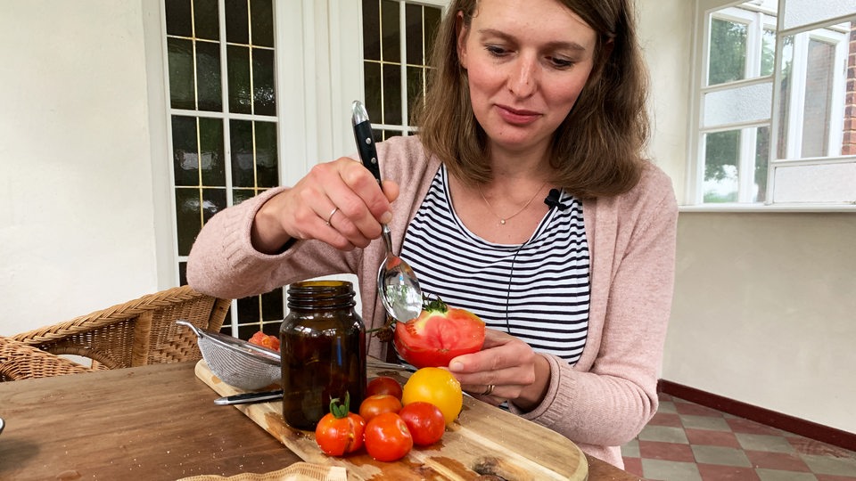 Eine Frau löffelt Samen aus einer Tomate
