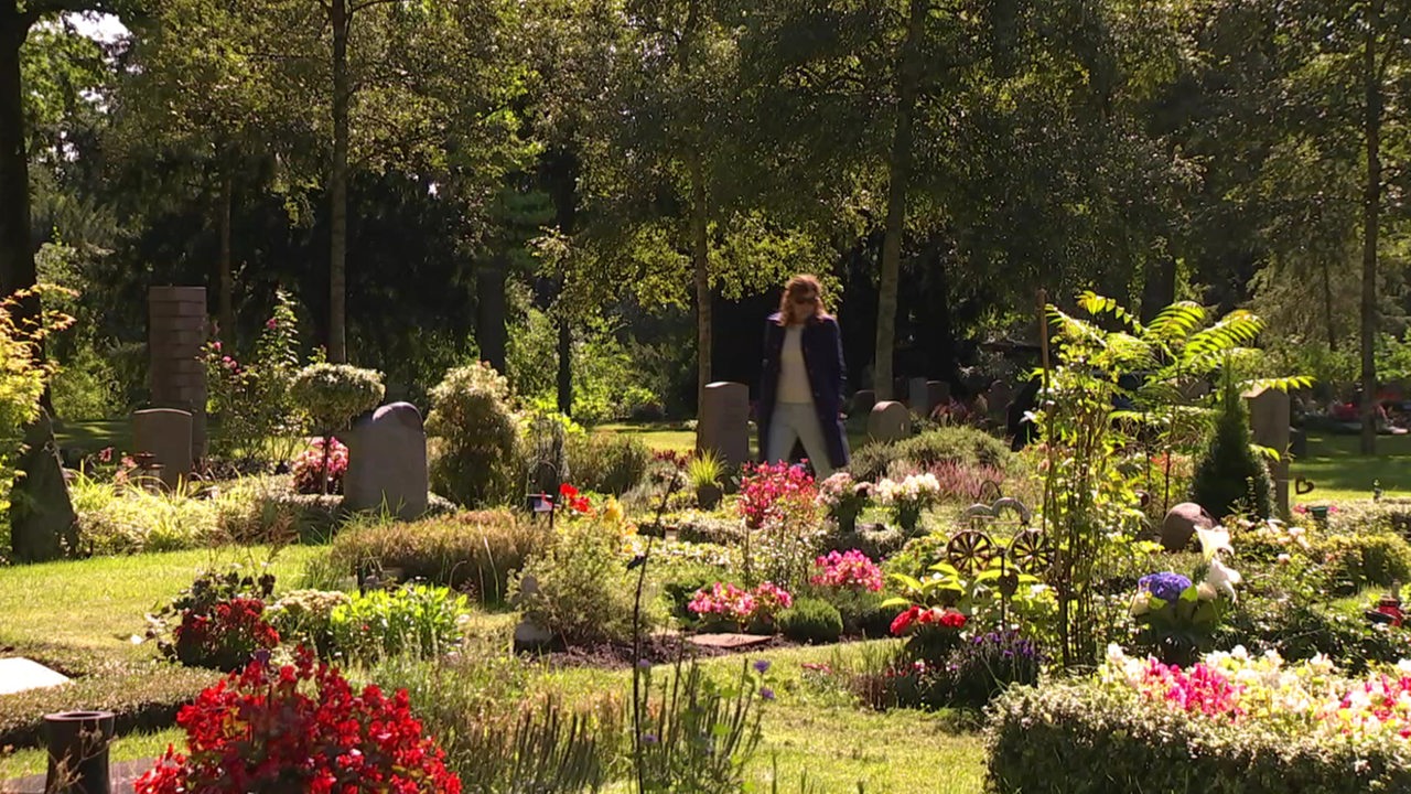 Eine Frau geht über den Osterholzer Friedhof spazieren und schaut sich die gepflegten Gräber an.