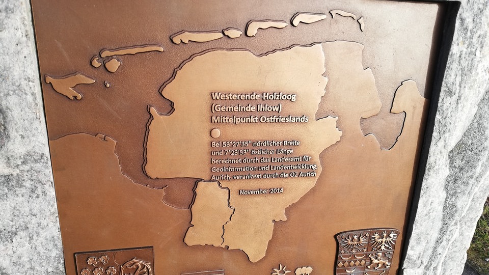 eine Schrifttafel, darauf der Umriss von Ostfriesland und der geografische Mittelpunkt
