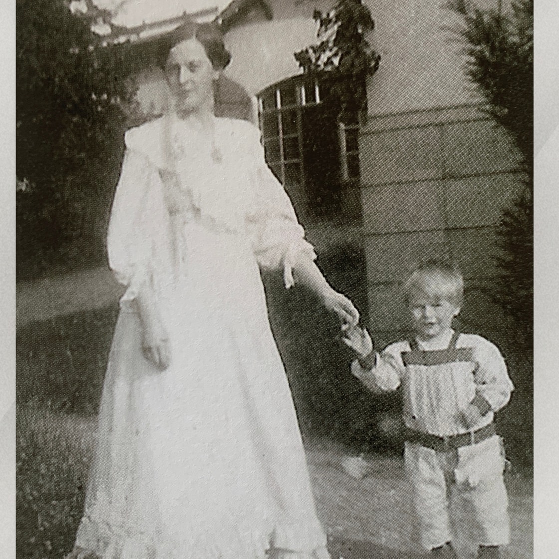 Eine schwarz-weiß Fotographie von Philine Vogeler in einem langen weißen Kleid mit einem Kind an der Hand