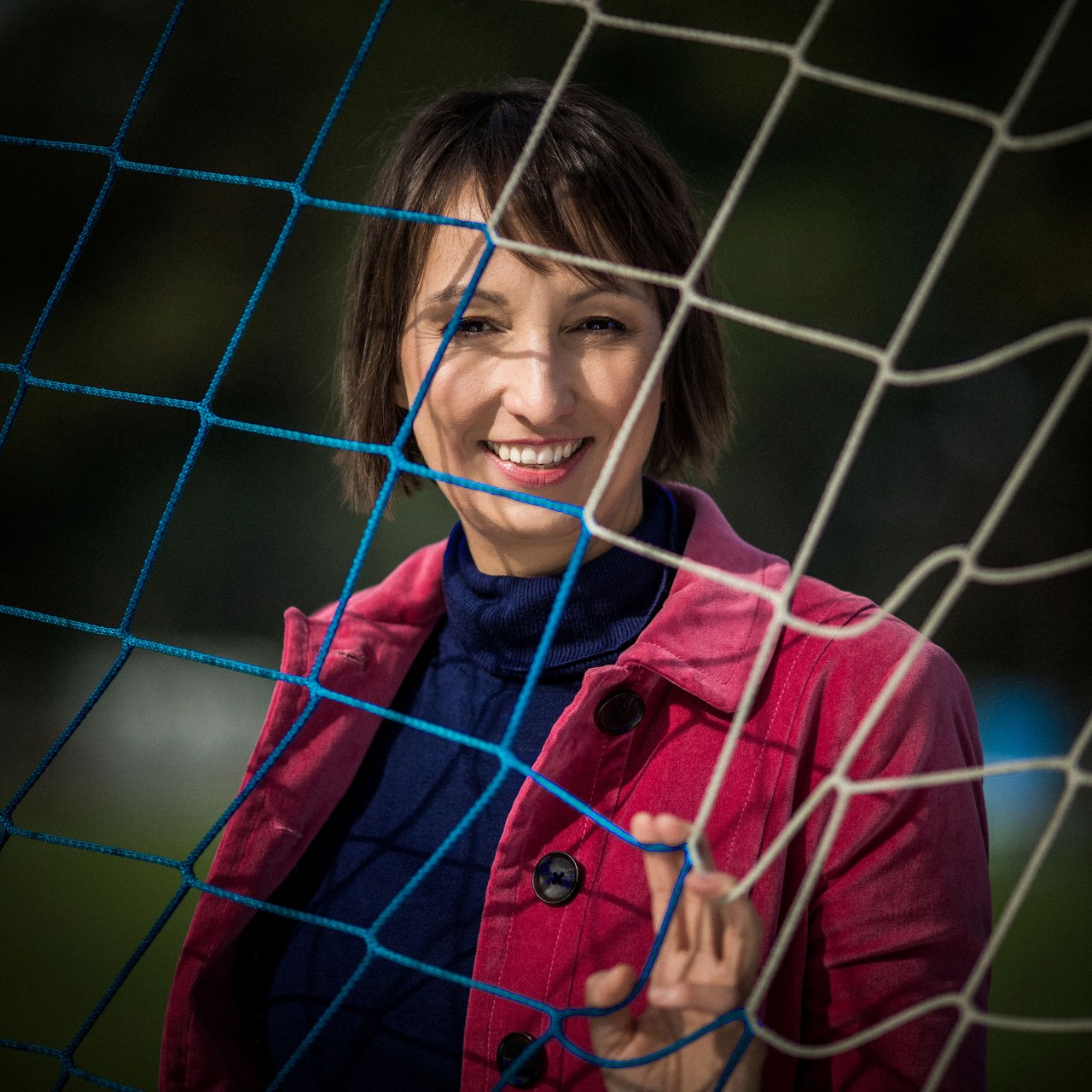 Eine Frau mit roter Jacke steht hinter einem Tornetz.