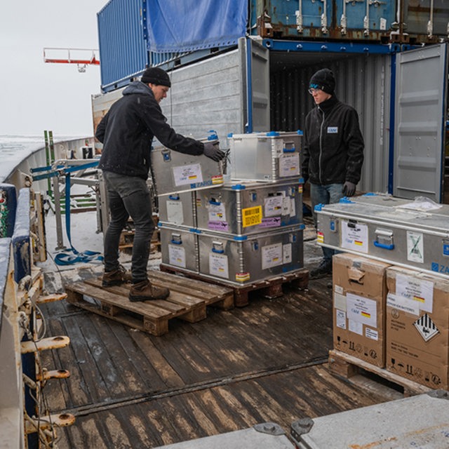 Zwei Besatzungsmitglieder der "Polarstern" verpacken Kisten in Container