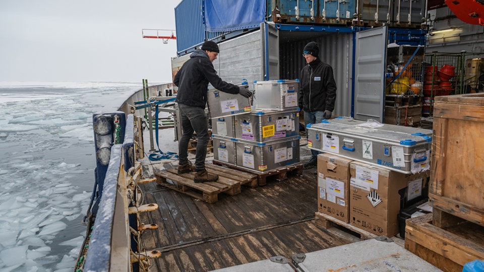 Zwei Besatzungsmitglieder der "Polarstern" verpacken Kisten in Container