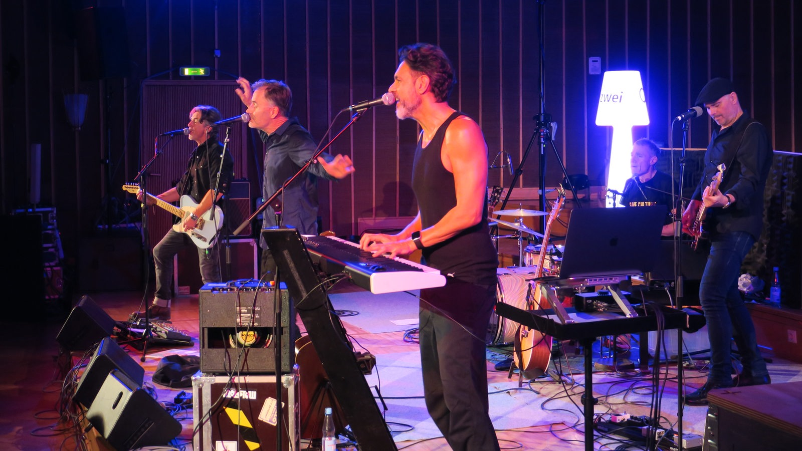 Fünf Männer mit Instrumenten stehen auf einer Bühne.