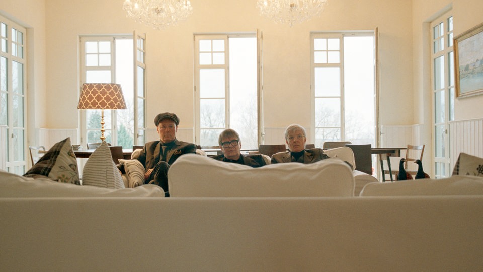 Drei Männer sitzen auf einem Sofa in einem hellen Zimmer