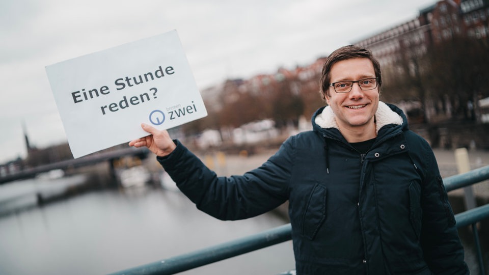 Ein Mann hält ein Schild auf dem steht: Eine Stunde reden