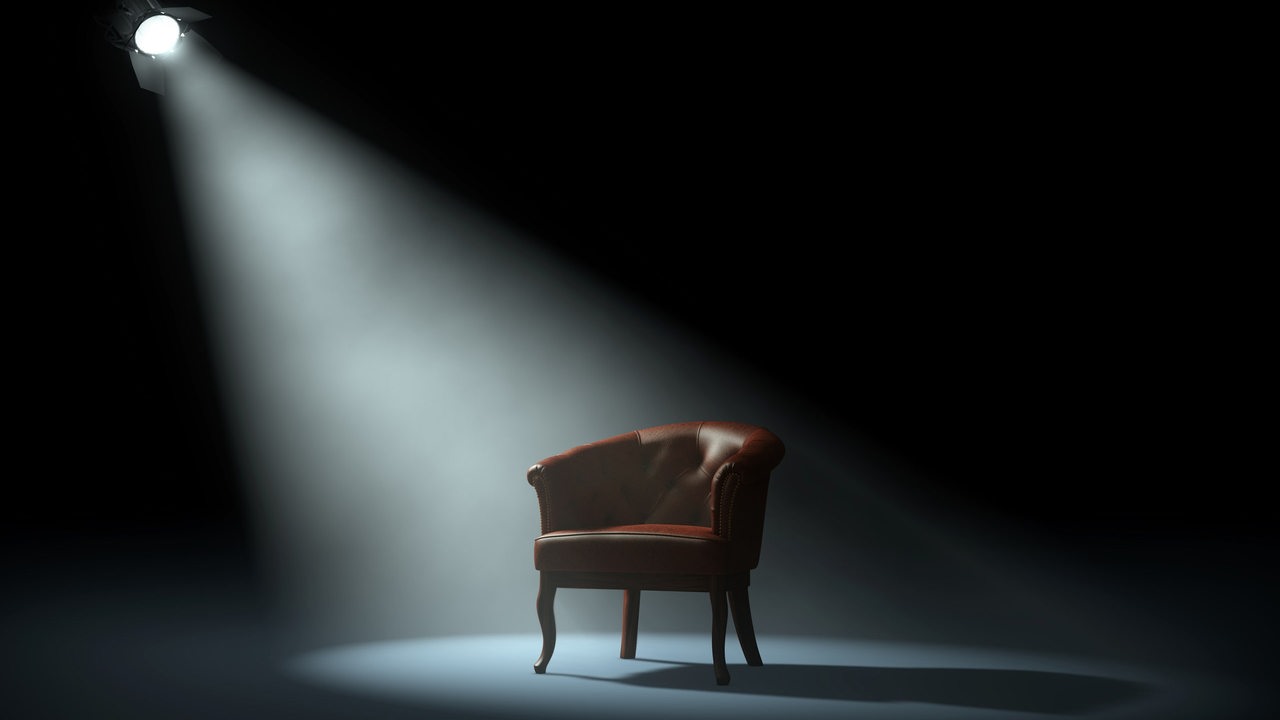Ein Sessel auf einer Bühne, angestrahlt von einem Scheinwerfer