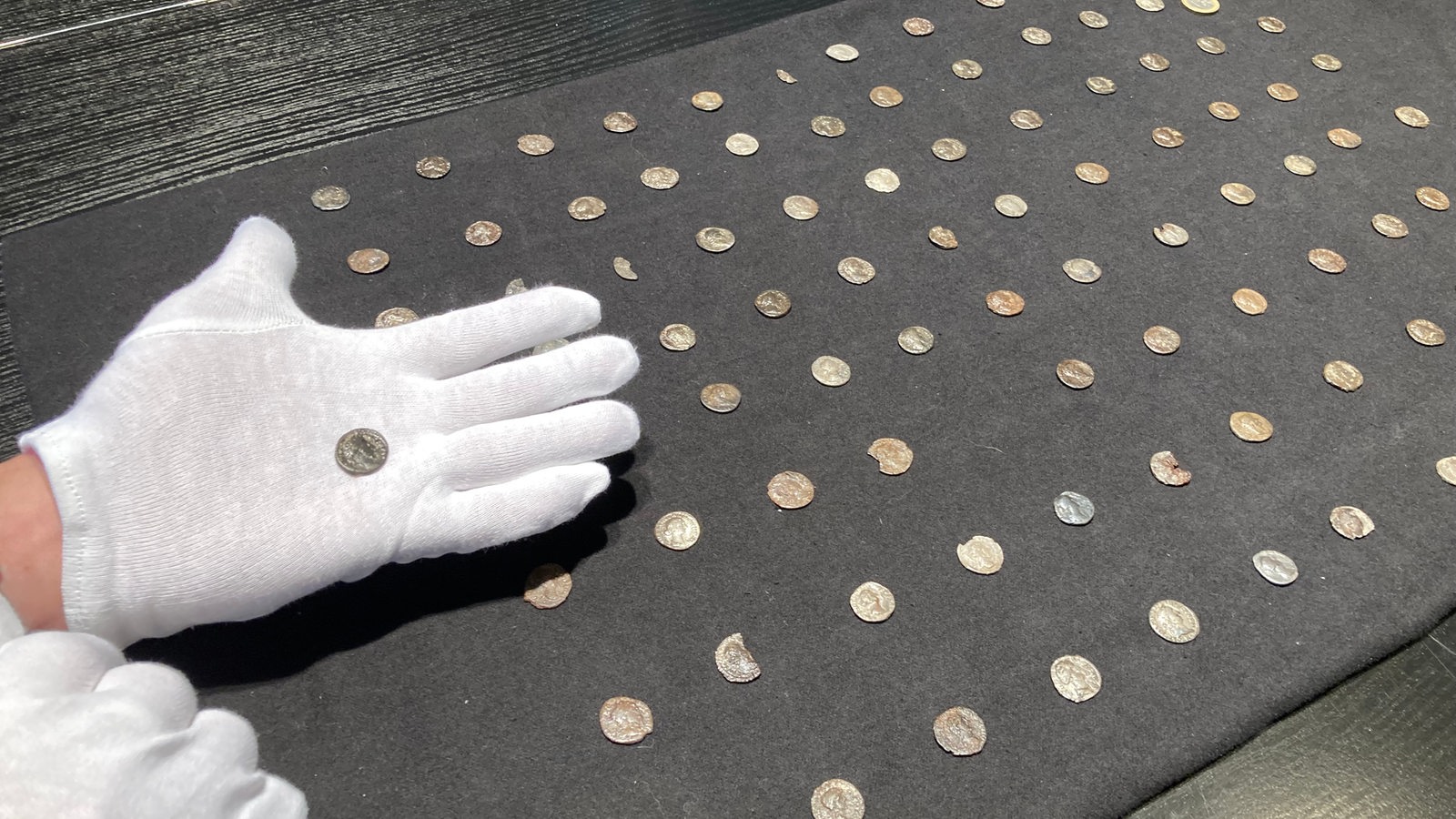 Person hält antike Münze in der Hand. Außerdem viele andere Münzen.