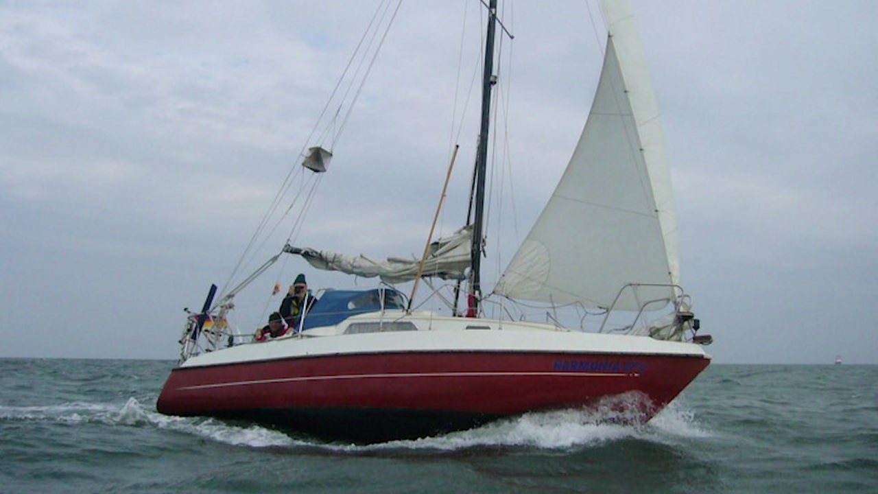 Ein rotes Segelboot mit Seglern fährt auf offenem Meer.