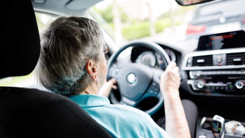 Eine über 90-jährige Frau sitzt hinter dem Lenkrad eines Autos.
