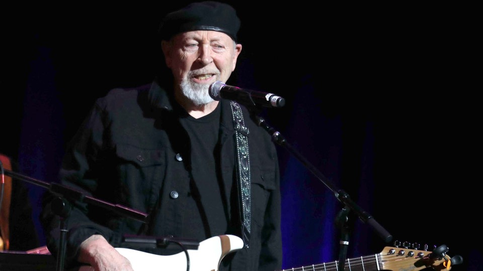 Richard Thompson mit Gitarre singt ins Mikrofon.