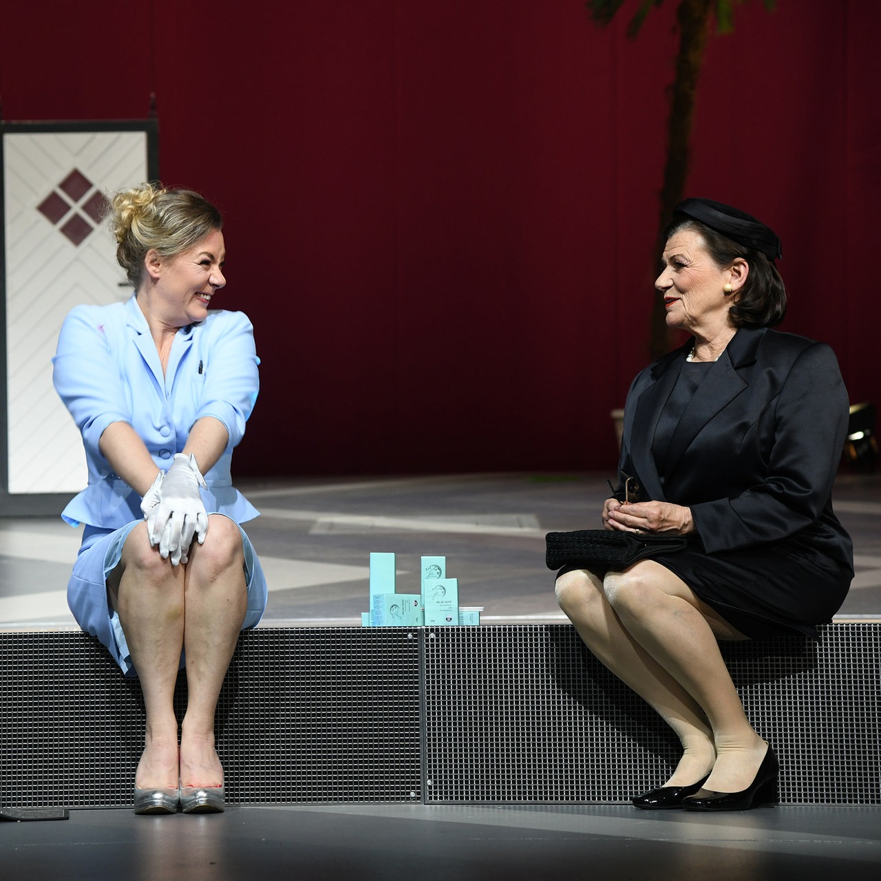 Zwei Schauspielerinnen sitzen auf der Bühne und unterhalten sich freudig