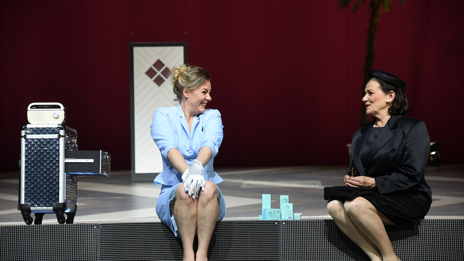 Zwei Schauspielerinnen sitzen auf der Bühne und unterhalten sich freudig