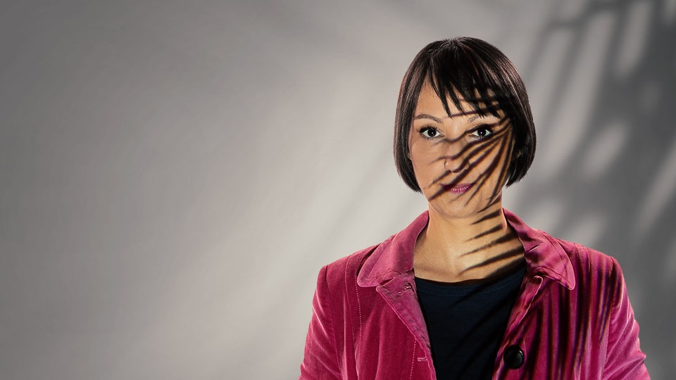 Eine Frau, deren Gesicht halb von einem Palmenzweig beschattet wird.