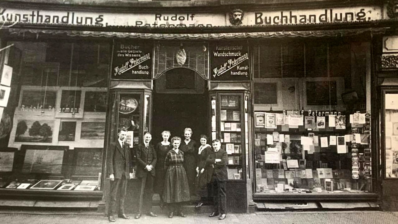 Schwarzweiß-Bild: eine Gruppe Menschen steht vor einer Buchhandlung