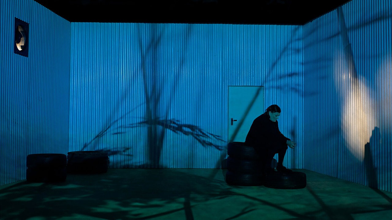 Schauspieler auf der Bühne im Stück "Tom auf dem Lande" in einem dunkelblau ausgeleuchteten Raum