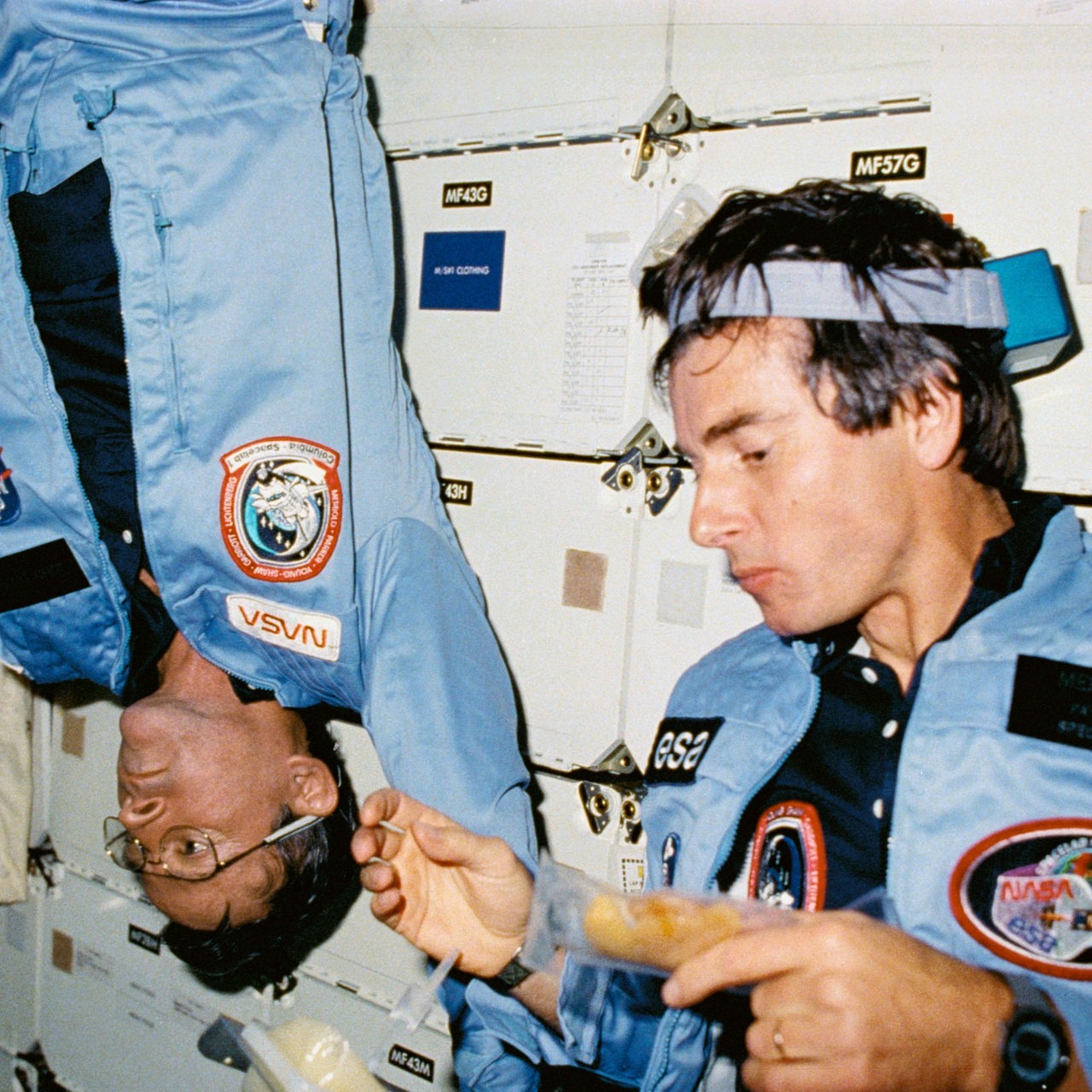 Die Astronauten John W. Young und Ulf Merbold bei einer Weltraummahlzeit im Space Shuttle Columbia.