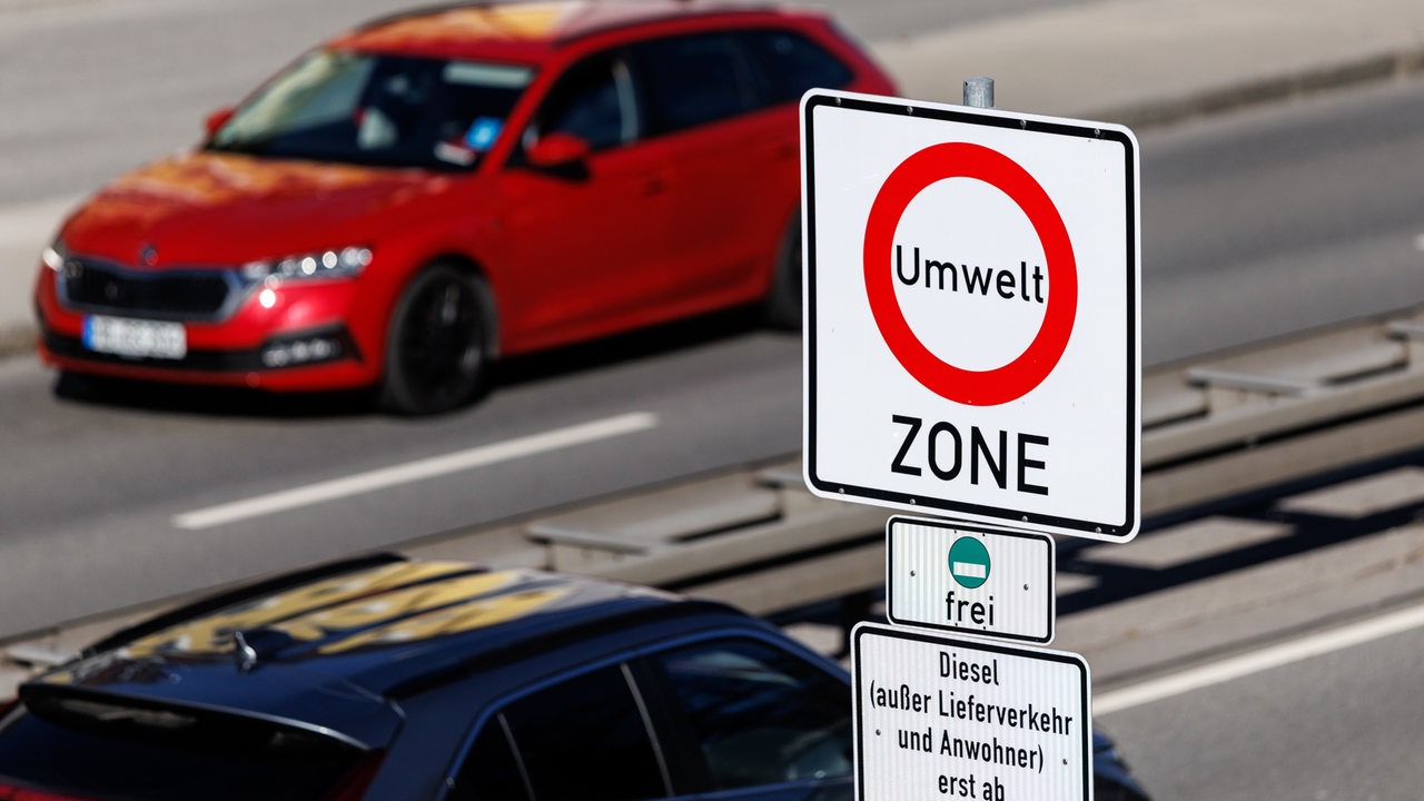 Ein Schild weist auf eine Umweltzone hin. Im Hintergrund fährt ein rotes Auto.
