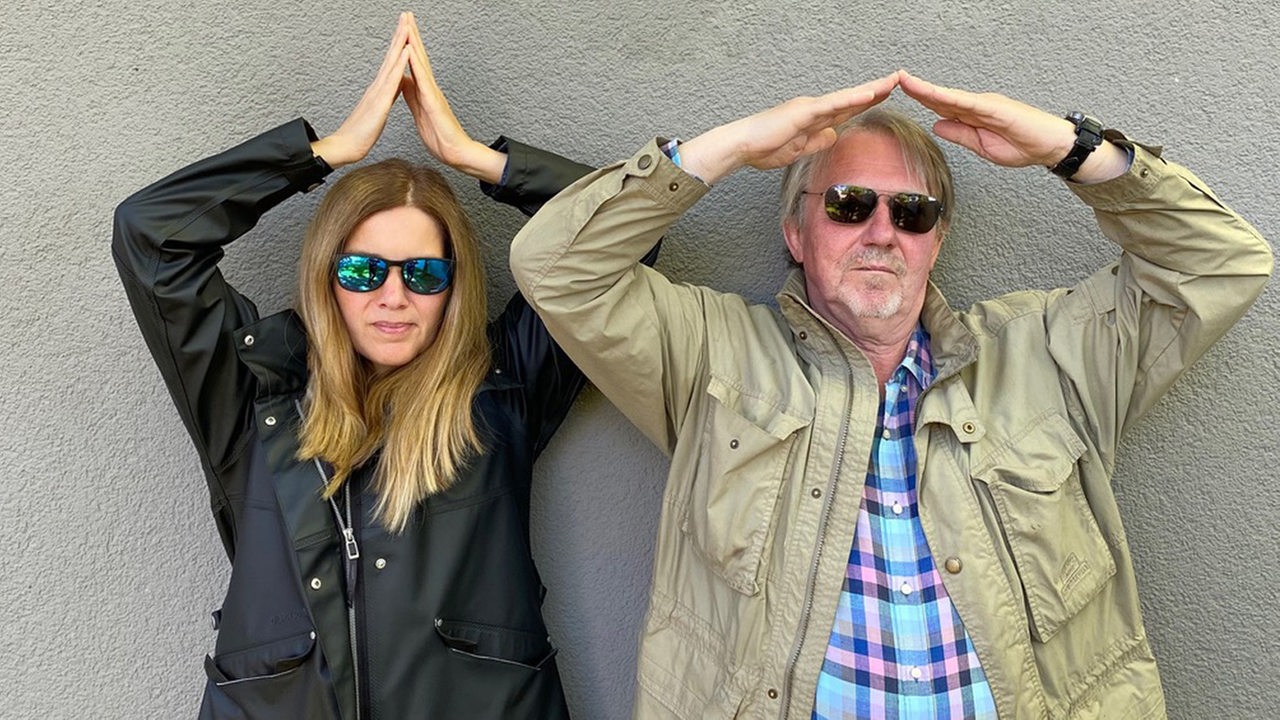 Tina Voß und Dietmar Wischmeyer formen mit gefalteten Händen ein Hausdach über ihren Köpfen