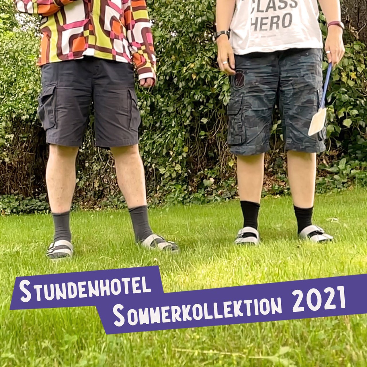 Die Beine von zwei Personen mit Bermuda-Shorts, Socken und Birkenstock-Sandalen.