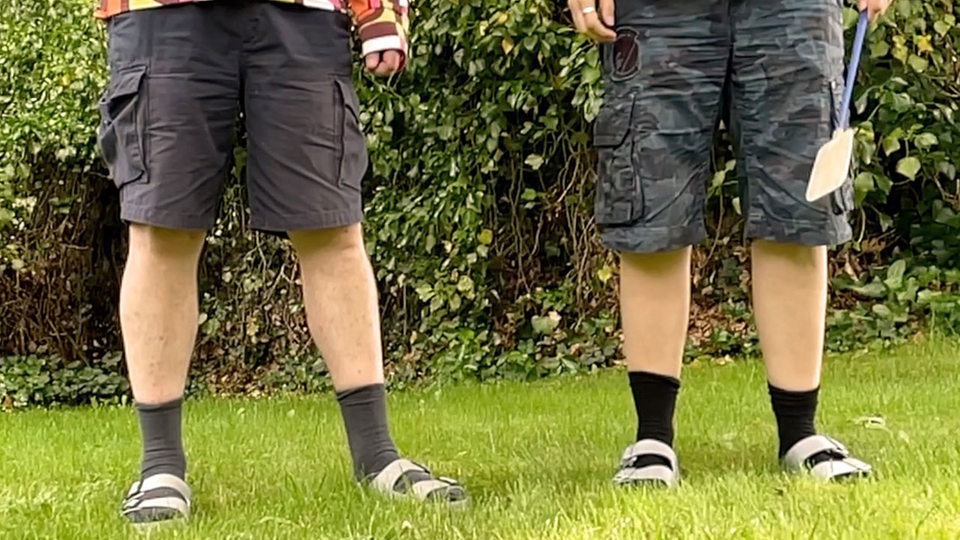 Die Beine von zwei Personen mit Bermuda-Shorts, Socken und Birkenstock-Sandalen.