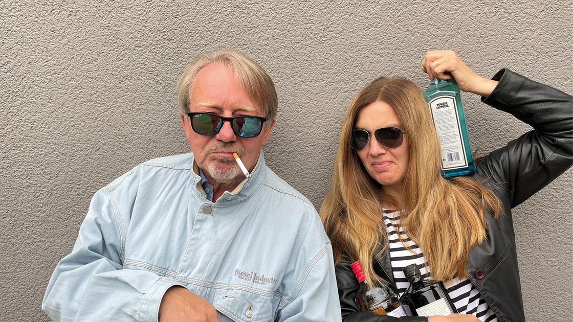 Dietmar Wischmeyer mit Zigarette im Mund und Tina Voß mit einer Flasche Alkohol in der Hand.