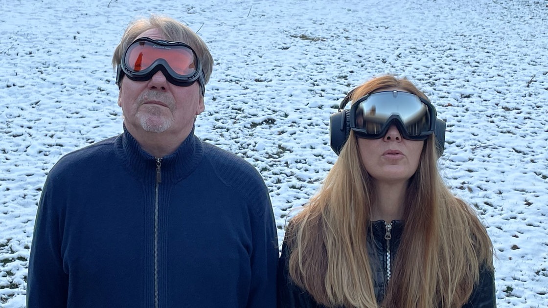 Dietmar Wischmeyer  und Tina Voß stehen im Schnee, sie tragen Ski-Brillen und gucken nach oben