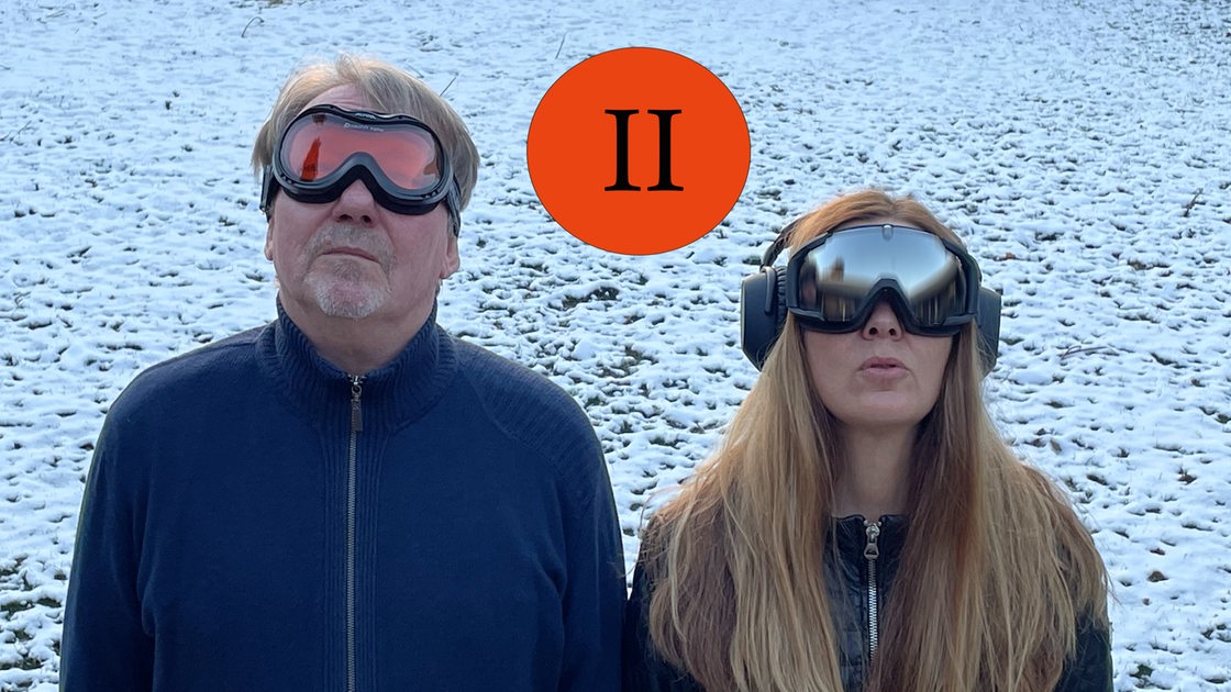 Dietmar Wischmeyer und Tina Voß stehen im Schnee, tragen Skibrillen und blicken in den Himmel.
