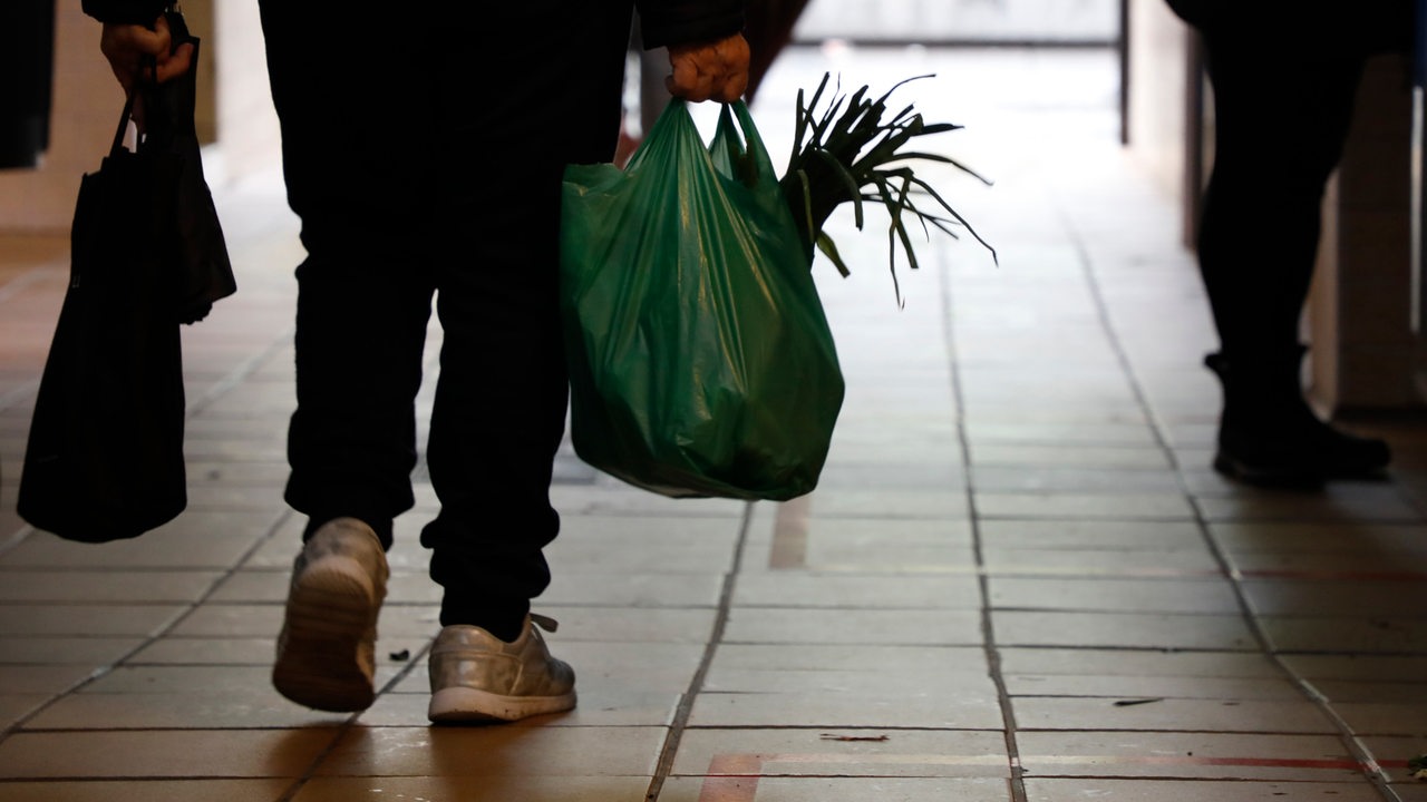 Ein Mann in Turnschuhen trägt Einkaufstüten mit Gemüse. Rückansicht