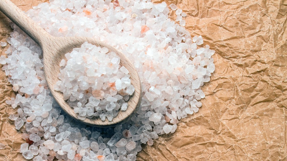 Ein Holzlöffel gefüllt mit Salz über einem Salzhaufen (Symbolbild)